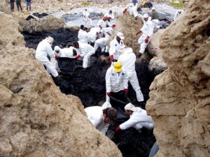 People in HAZMAT suits cleaning up a coastal oil spill. 