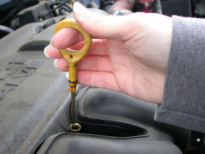 A woman checking her car oil with a dipstick